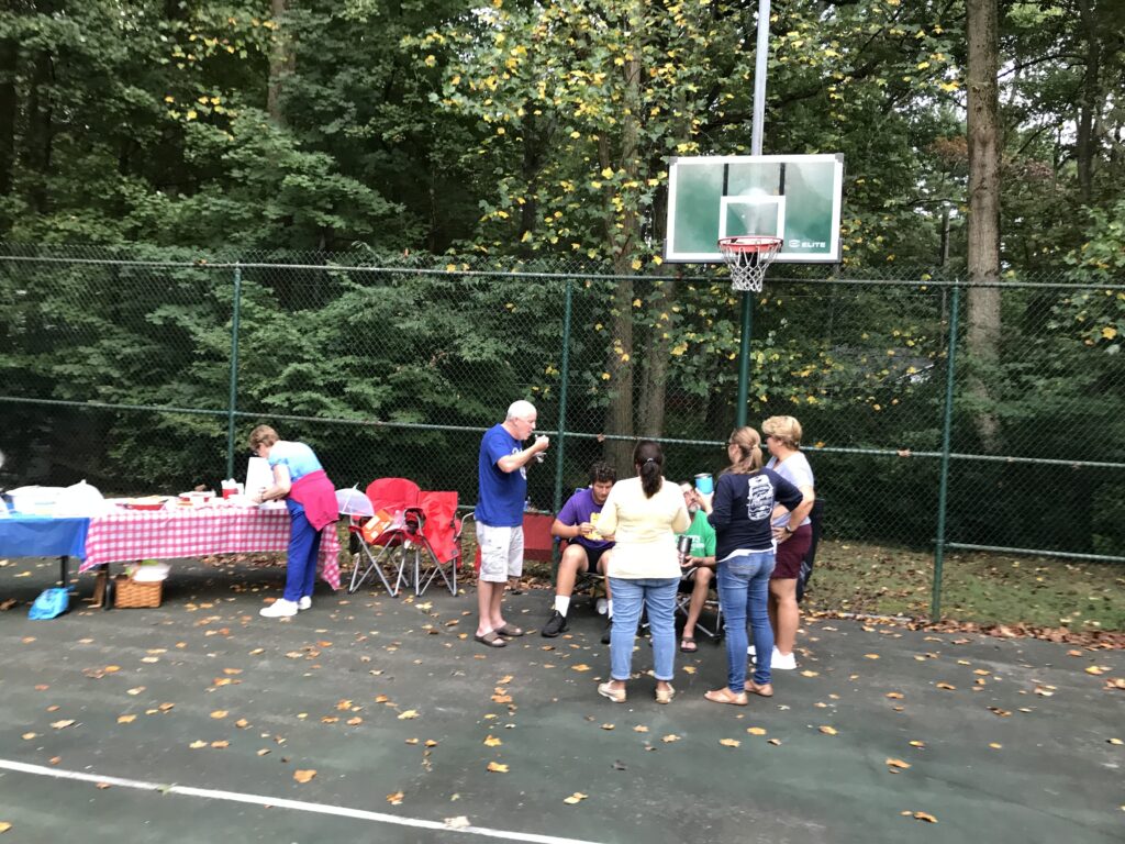 A group of people standing around an outdoor basketball court.